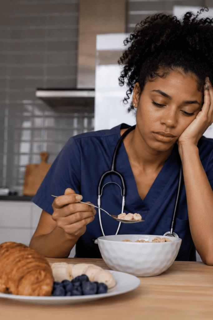 Exhausted nurse in scrubs staring blankly at her breakfast, showing sings of nurse burnout and loss of appetite